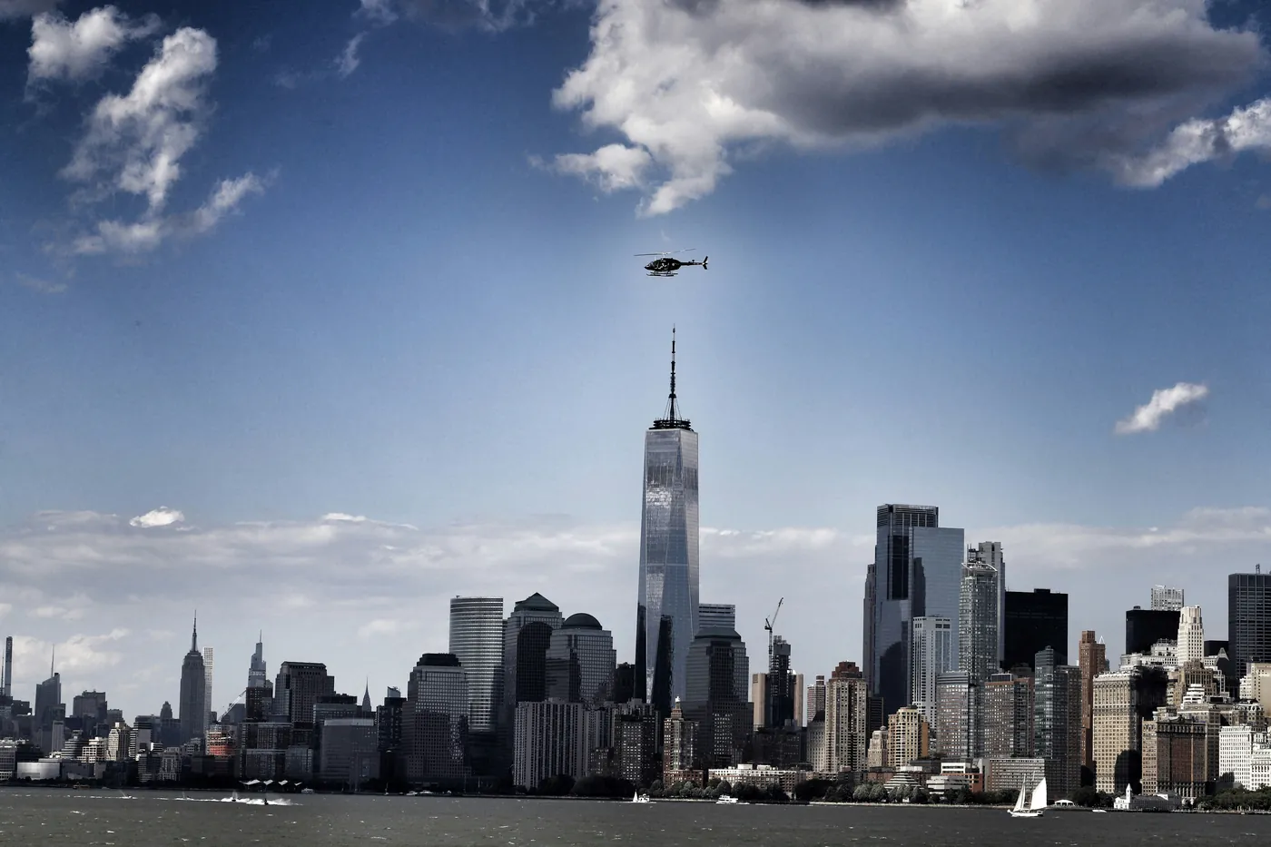 Helicopter passing One World Trade Center against a blue sky with white clouds — Lower Manhattan view